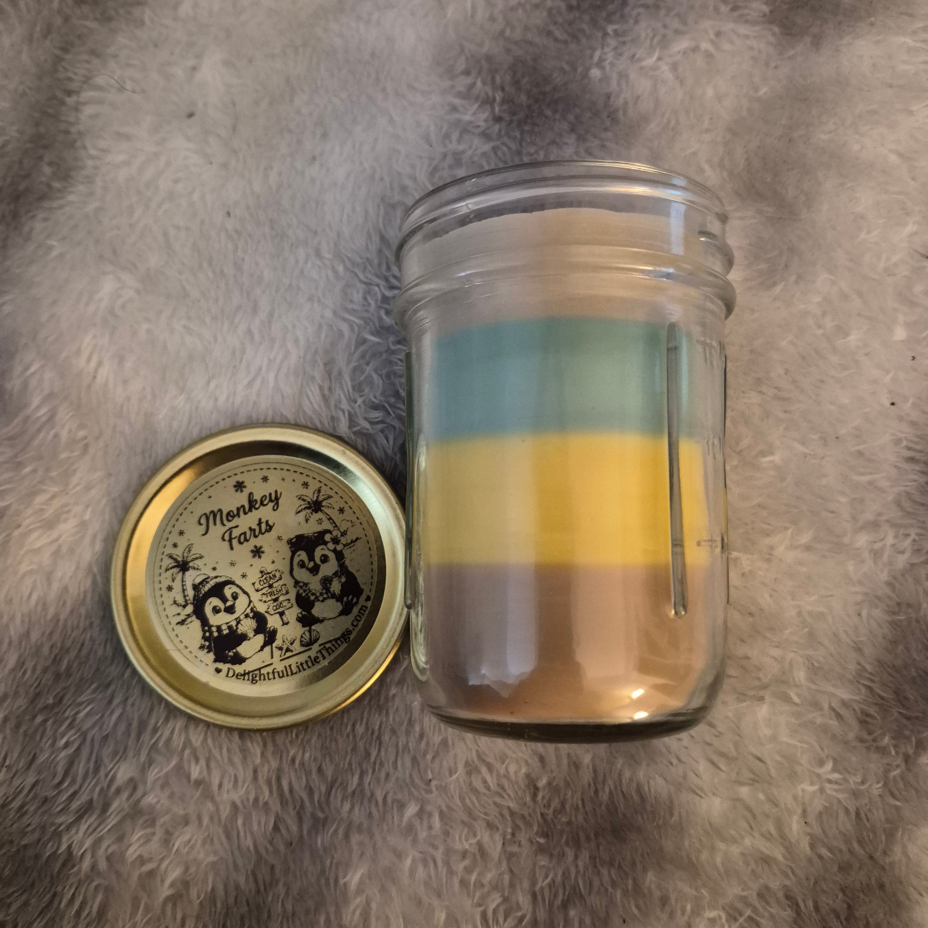 "9oz Monkey Farts scented handmade candle in glass jar with black lid, light green layered wax and Delightful Little Things Butt Naked label with penguin beach scene, DelightfulLittleThings.com"